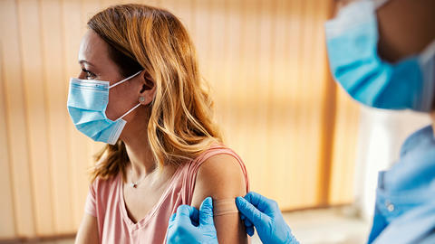 Frau mit Mundschutz bekommt eine Imfpung