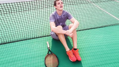 Tennisspieler sitzt erschöpft auf dem Spielfeld