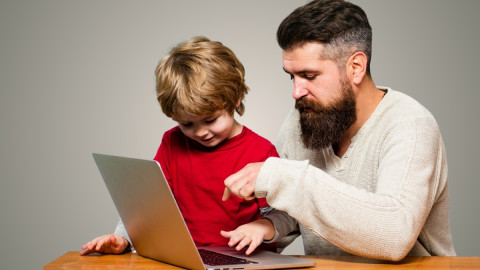Vater zeigt Sohn etwas auf Laptop-Tastatur.