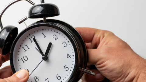 Person dreht an dem Wecker und stellt die Uhr um.