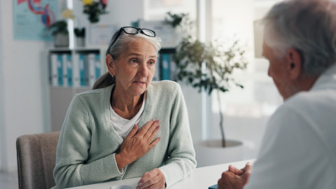 Frau ist beim Arztgespräch und fasst sich an die Brust